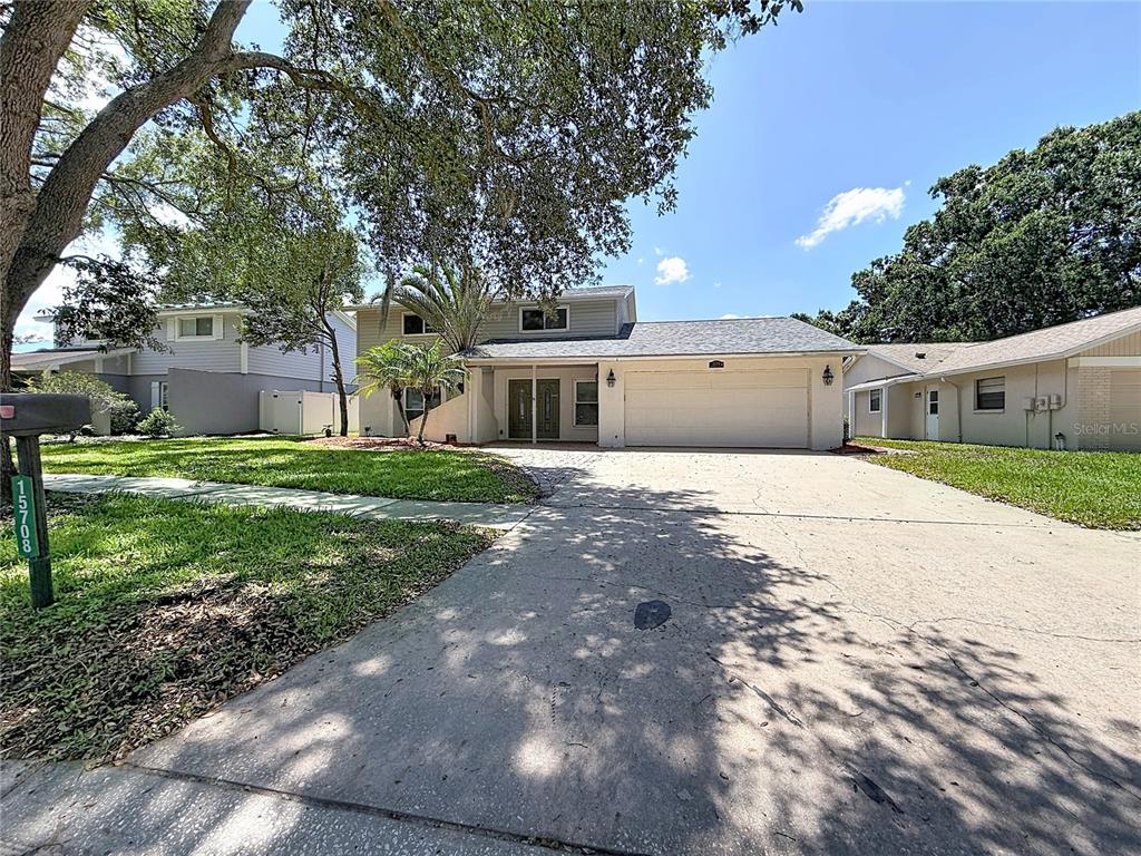 A two-story house with a large concrete driveway, a two-car garage, and mature trees — 15708 WOODCOCK PLACE, TAMPA, FL