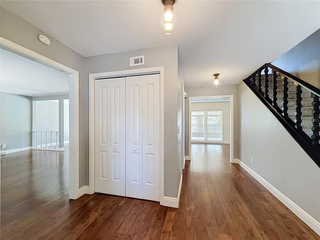 An interior view of a home entryway with wood flooring, a staircase, and closet doors — 15708 WOODCOCK PLACE, TAMPA, FL
