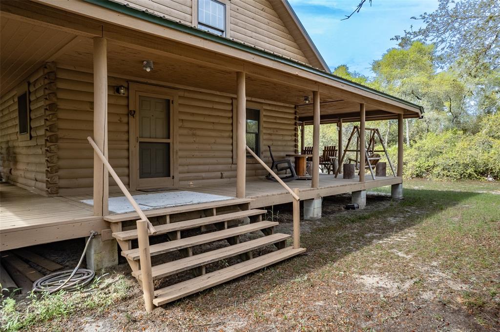 A log cabin exterior features a wide covered porch with wooden steps and outdoor seating — 20259 NE 147TH TERRACE, FORT MC COY, FL