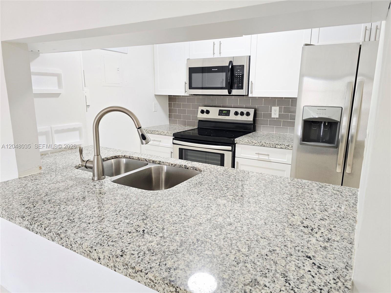 A kitchen features granite countertops, stainless steel appliances, white cabinets, and a gray tile backsplash — 8877 Fontainebleau Blvd # 202, Miami FL 33172, MIAMI, FL