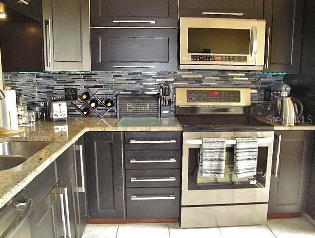 A kitchen features dark cabinetry, stainless steel appliances, and a tiled backsplash — 6294 BAHIA DEL MAR CIRCLE UNIT 215, ST PETERSBURG, FL