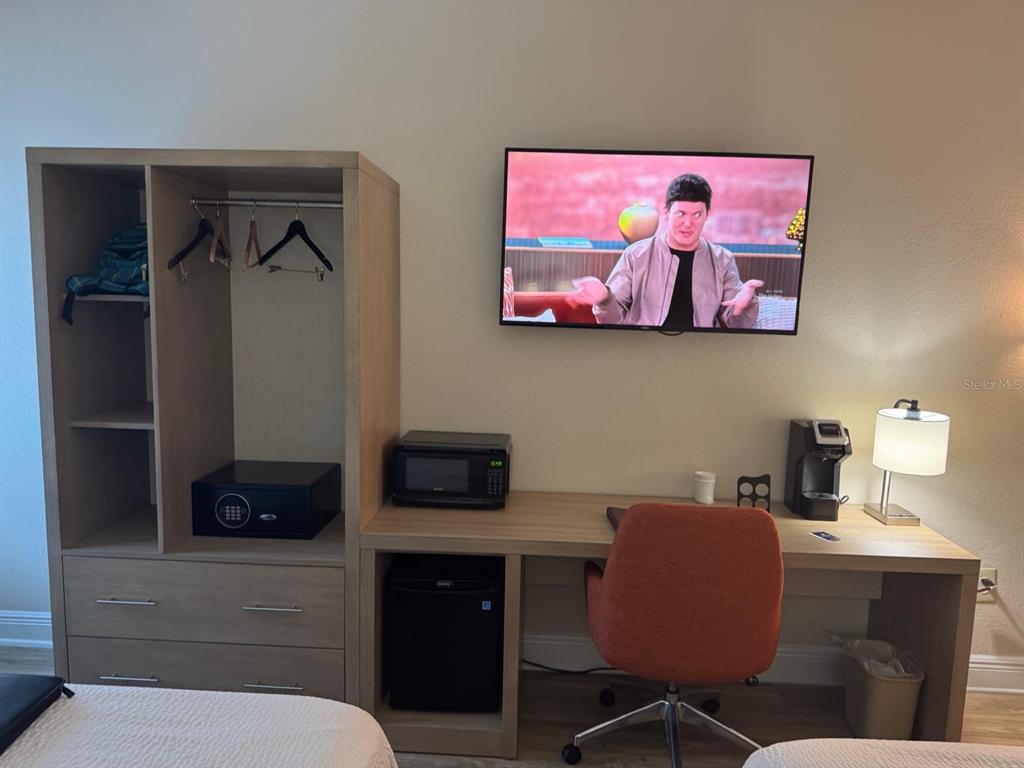 A hotel room features a wooden wardrobe, desk, television, mini-fridge, microwave, and an orange chair — 3000 MAINGATE LN UNIT 319, KISSIMMEE, FL