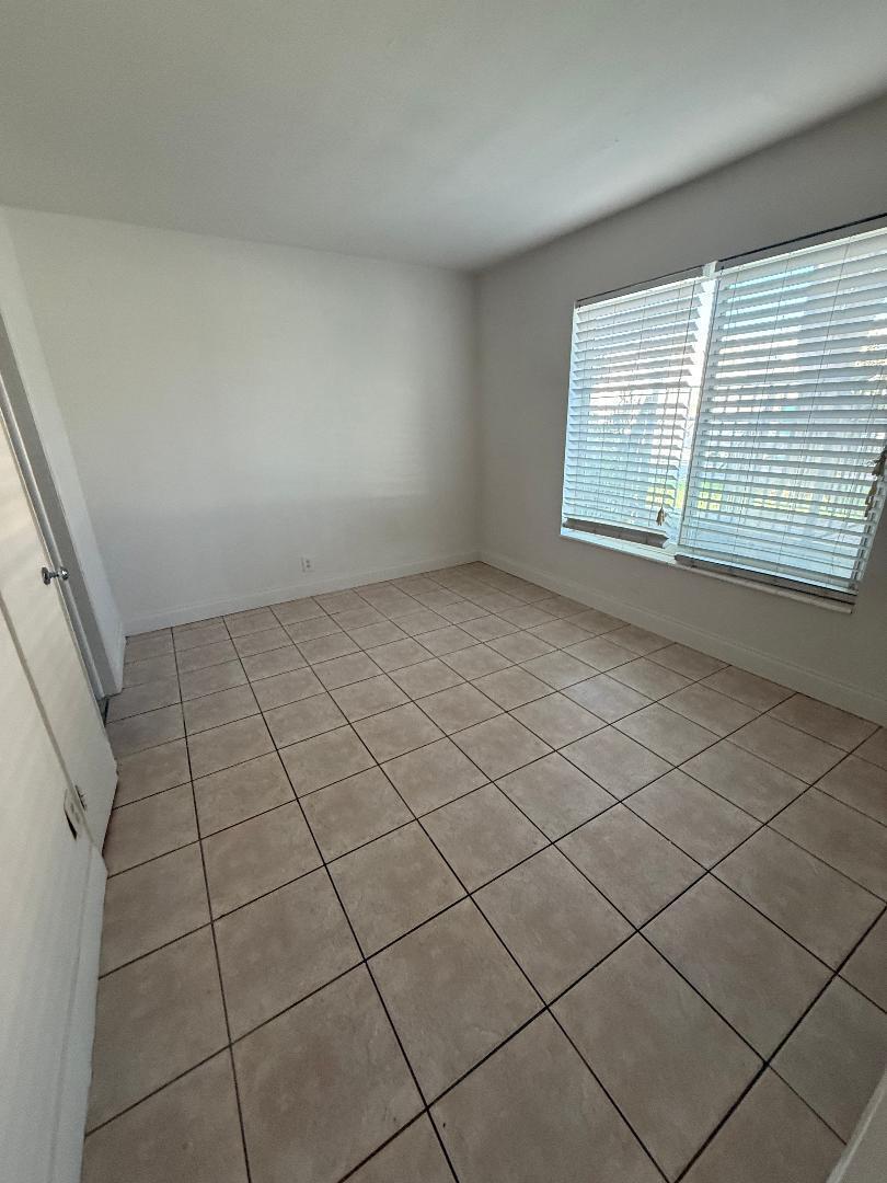 An empty room features beige tile flooring, white walls, and a window with white blinds — 2317 NE 2nd Street # 1, Pompano Beach FL 33062, POMPANO BEACH, FL