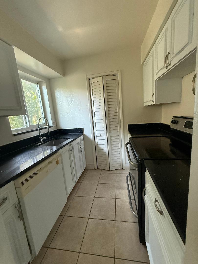 A galley kitchen features white cabinets, black countertops, tile flooring, and a white dishwasher — 2317 NE 2nd Street # 1, Pompano Beach FL 33062, POMPANO BEACH, FL