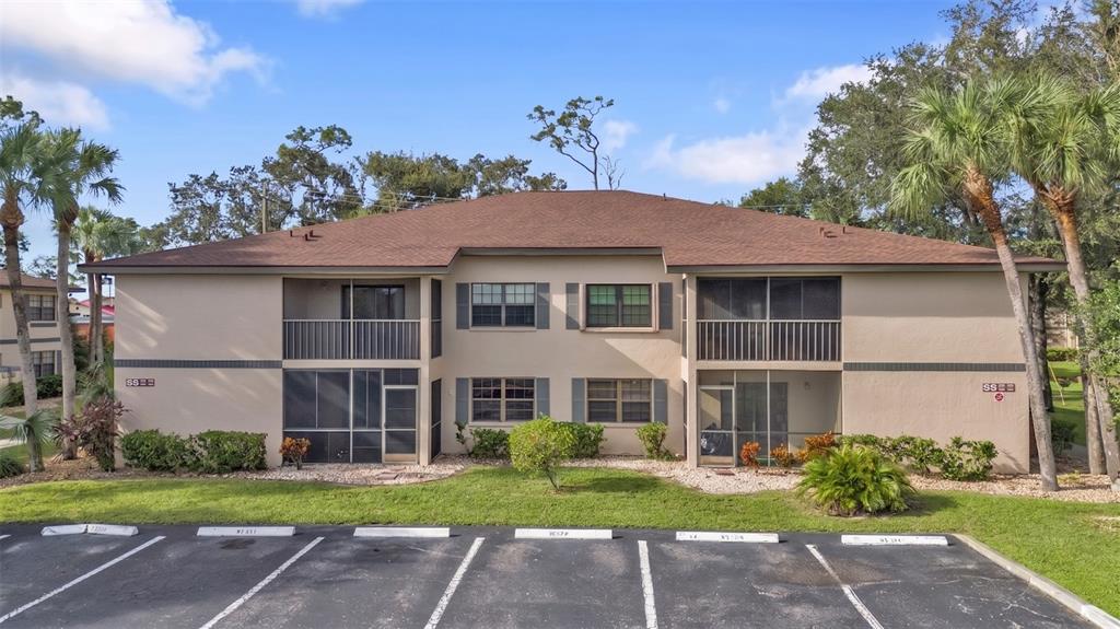 A two-story apartment building with tan stucco walls, a brown roof, and screened-in balconies — 19505 QUESADA AVENUE UNIT SS103, PORT CHARLOTTE, FL