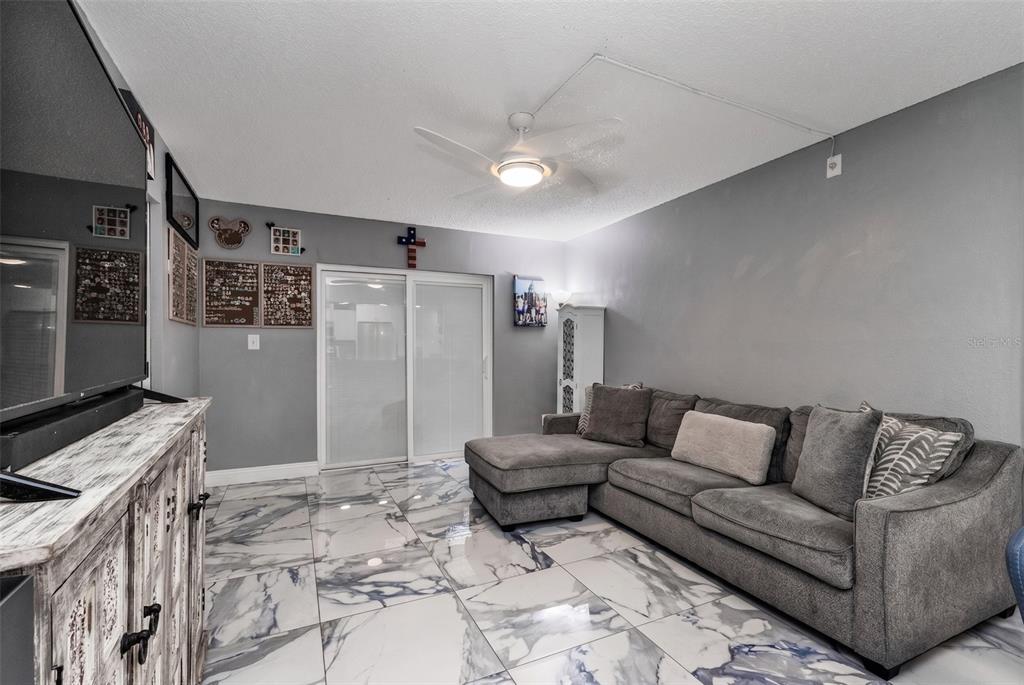 A living room features a grey sectional sofa, marble-patterned tile floors, and a ceiling fan — 19505 QUESADA AVENUE UNIT SS103, PORT CHARLOTTE, FL
