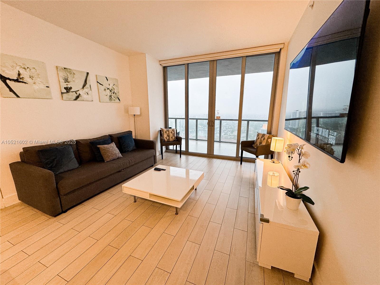 A living room features a dark sofa, white coffee table, and floor-to-ceiling windows with balcony access — 2600 E Hallandale Beach # 3104, Hallandale Beach FL 33009, HALLANDALE BEACH, FL
