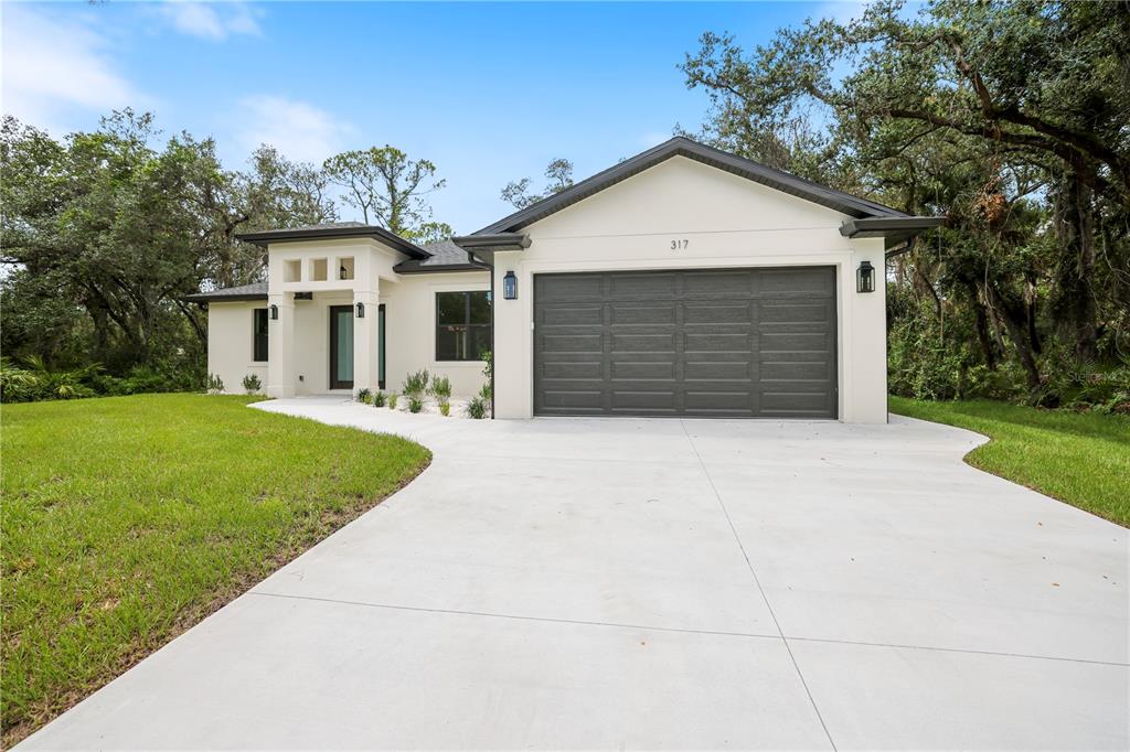 A modern single-story house with a white exterior, dark garage door, and a concrete driveway — 317 DORMAN STREET, PORT CHARLOTTE, FL