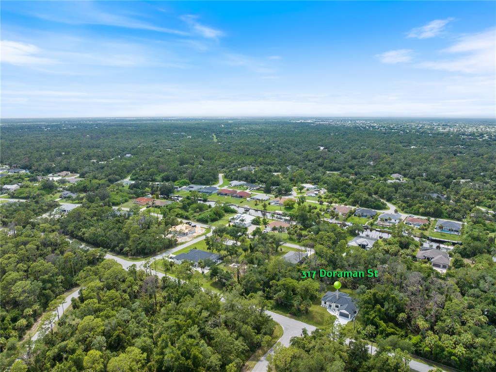 An aerial view shows a single-family home surrounded by dense trees and nearby canals — 317 DORMAN STREET, PORT CHARLOTTE, FL