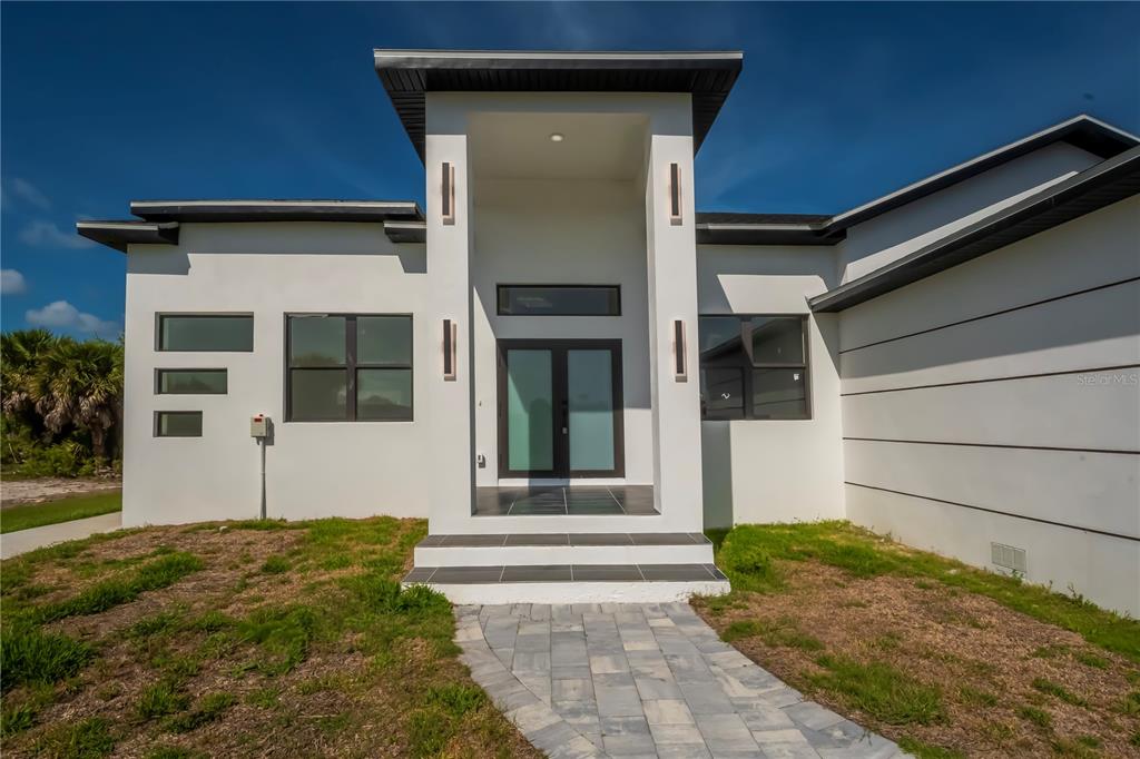 The exterior of a modern white house features a covered entryway with double glass doors — 10165 & 10157 KINGSVILLE DRIVE, PORT CHARLOTTE, FL