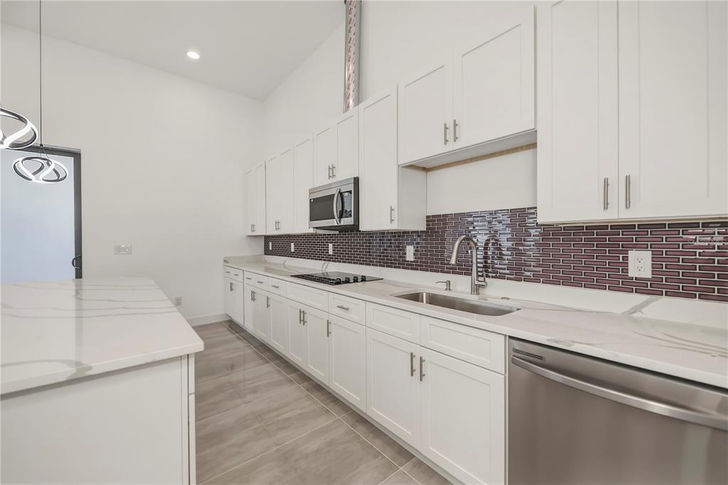 A modern kitchen features white cabinetry, a dark tile backsplash, and a white stone island — 10165 & 10157 KINGSVILLE DRIVE, PORT CHARLOTTE, FL