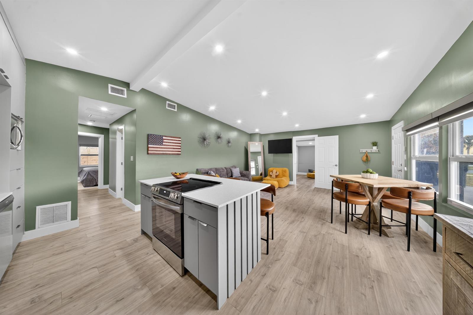 An open-concept kitchen and living area features sage green walls, light wood flooring, and an island — 801 SE 15th Street, Stuart FL 34994, STUART, FL