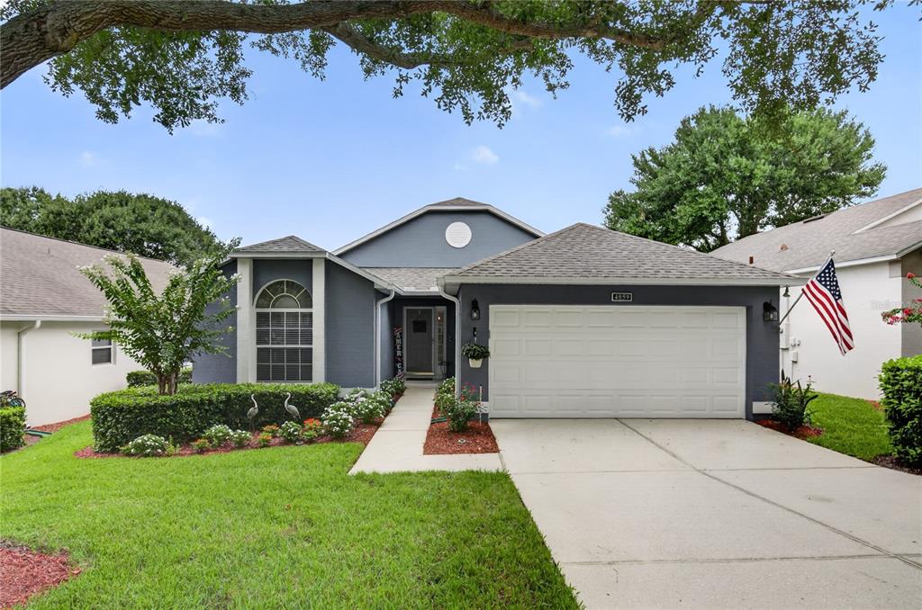 A gray house exterior features a front garden with a tree, hedge, and walkway — 4059 CAPLAND AVENUE, CLERMONT, FL