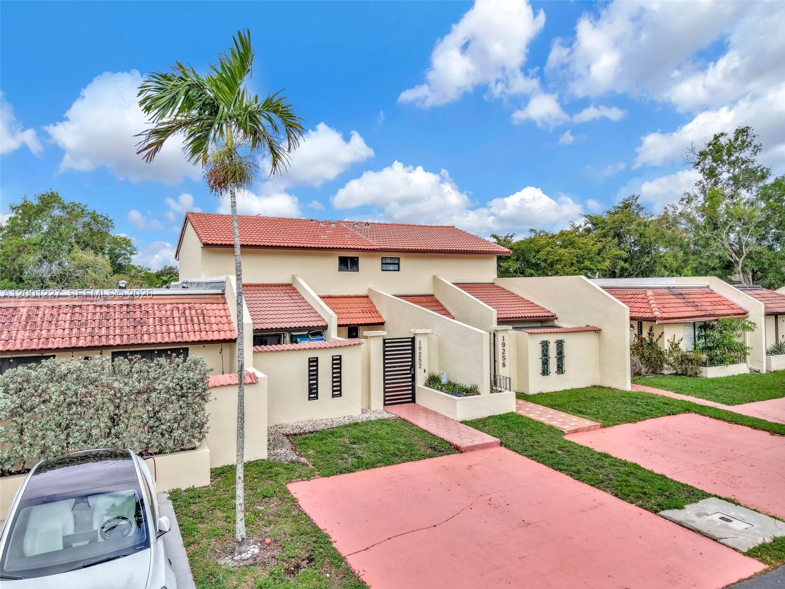 A two-story townhouse with a red tile roof, beige stucco walls, and a palm tree — 19252 NW 65th Ct, Hialeah FL 33015, HIALEAH, FL