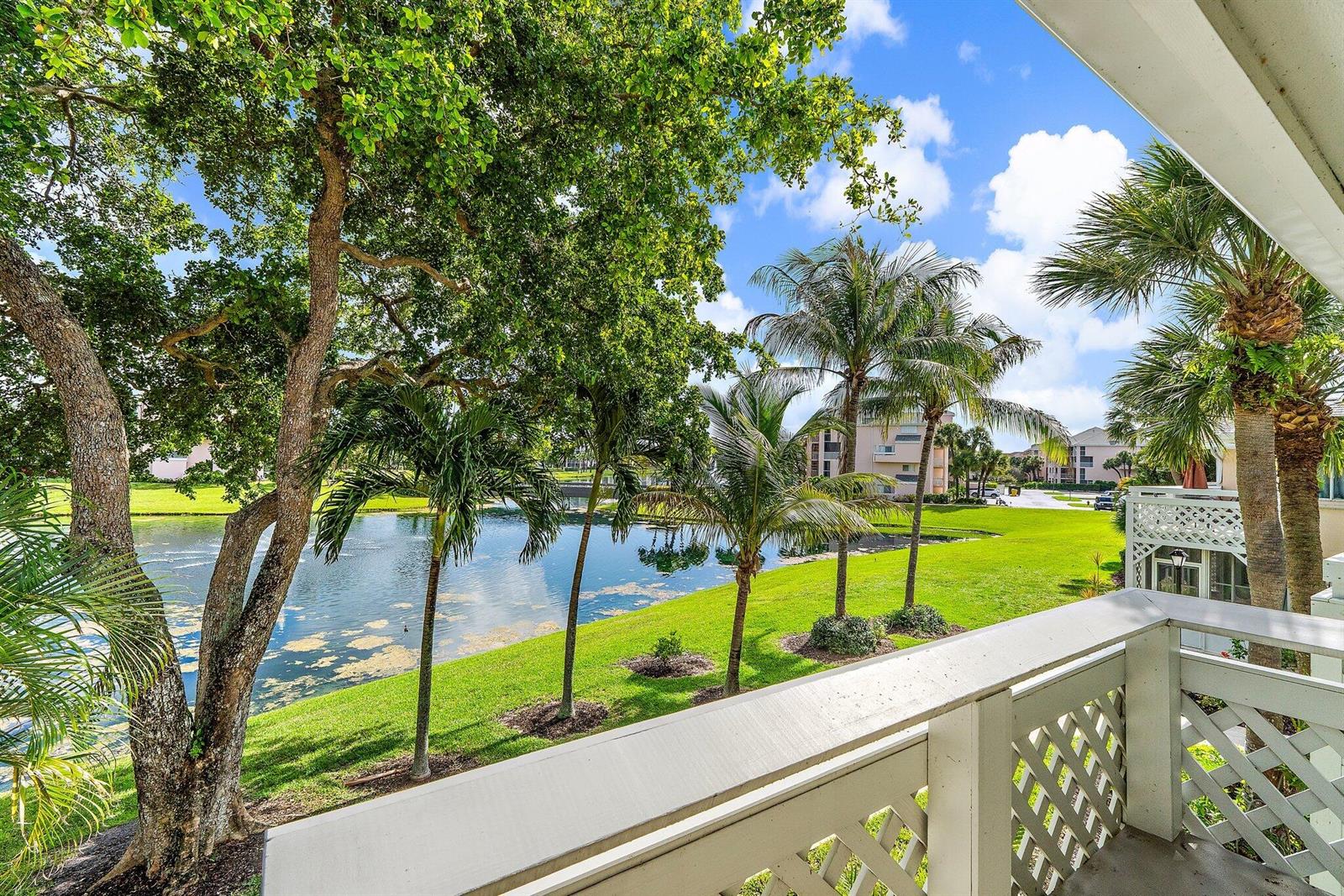 A view from a balcony overlooking a grassy lawn, a small pond, and palm trees — 353 S Us Hwy 1 # B8, Jupiter FL 33477, JUPITER, FL