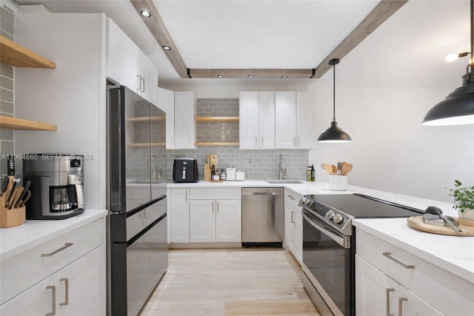 A modern kitchen features white cabinets, stainless steel appliances, gray subway tile, and wooden beams — 600 Three Islands Blvd # 1214, Hallandale Beach FL 33009, HALLANDALE BEACH, FL