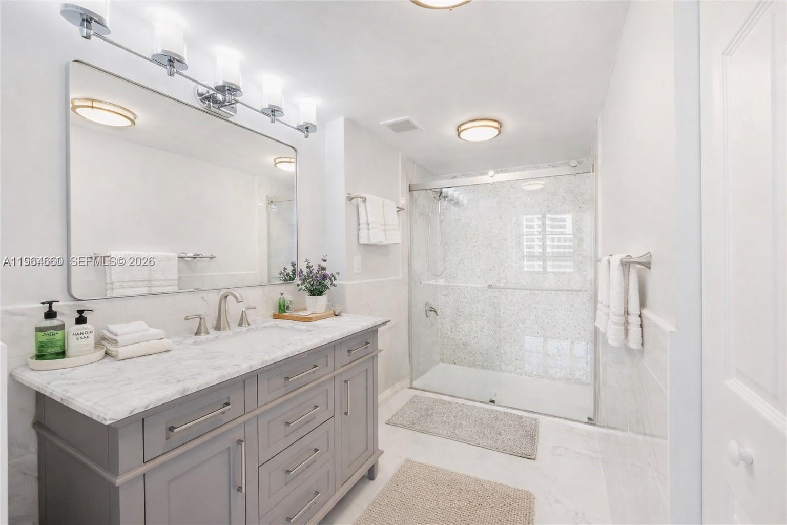 A bathroom features a gray vanity with a marble countertop, a mirror, and a glass shower — 600 Three Islands Blvd # 1214, Hallandale Beach FL 33009, HALLANDALE BEACH, FL