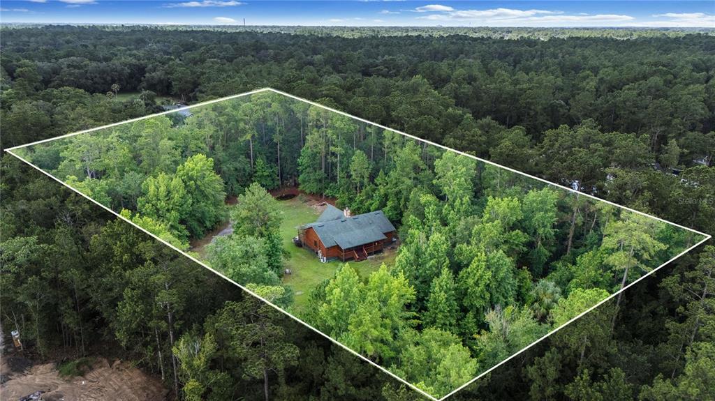An aerial view shows a wooden cabin nestled within a dense, forested lot — 712 MALLARD DRIVE, SANFORD, FL