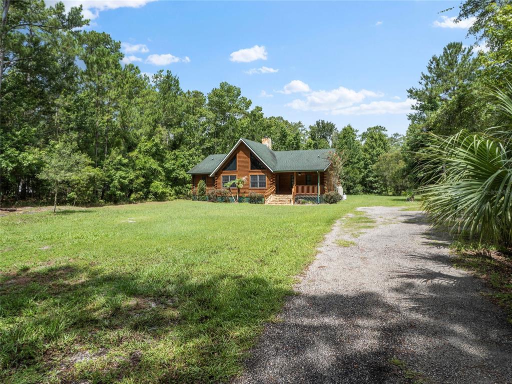 A log cabin home sits on a grassy lot with a gravel driveway and surrounding trees — 712 MALLARD DRIVE, SANFORD, FL