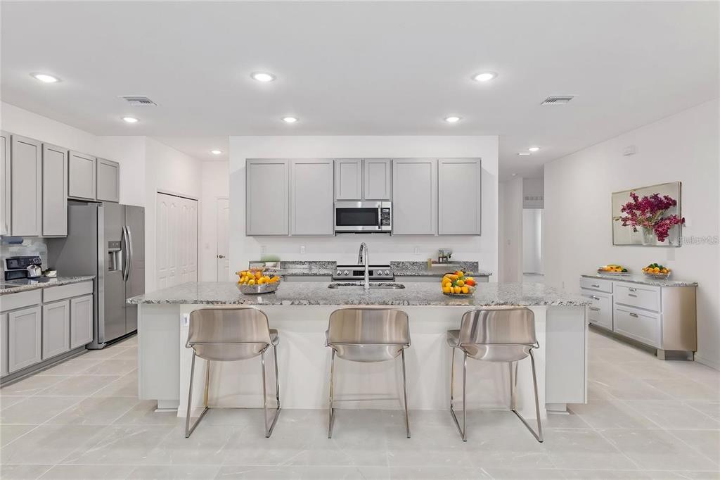 A modern kitchen features gray cabinetry, granite countertops, a central island, and three metal stools — 2275 NW 248TH WAY, NEWBERRY, FL