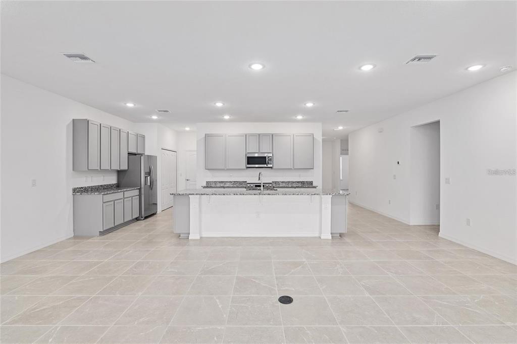 A modern kitchen features gray cabinets, granite countertops, a central island, and light tile flooring — 2275 NW 248TH WAY, NEWBERRY, FL