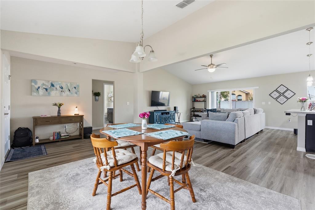 An open-concept living and dining area features light wood-look flooring and a vaulted ceiling — 13880 SW 45TH TERRACE, OCALA, FL