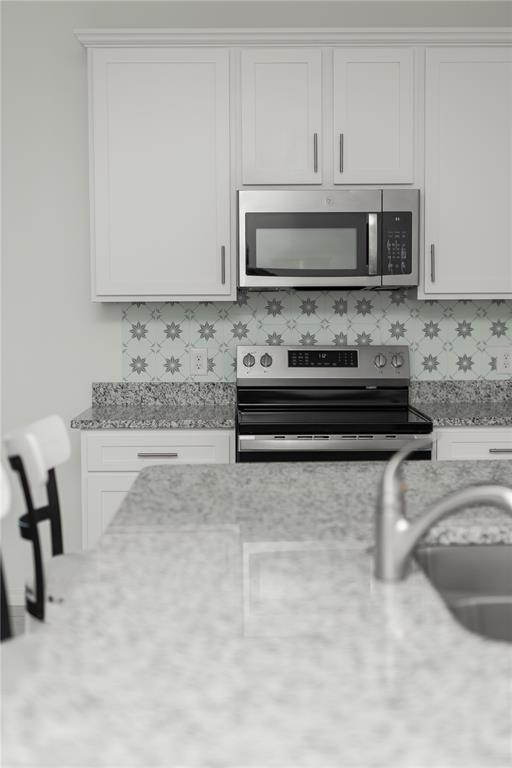 A kitchen features white cabinets, granite countertops, a stainless steel stove, and patterned tile backsplash — 661 CROWN ROSE DRIVE, EAGLE LAKE, FL