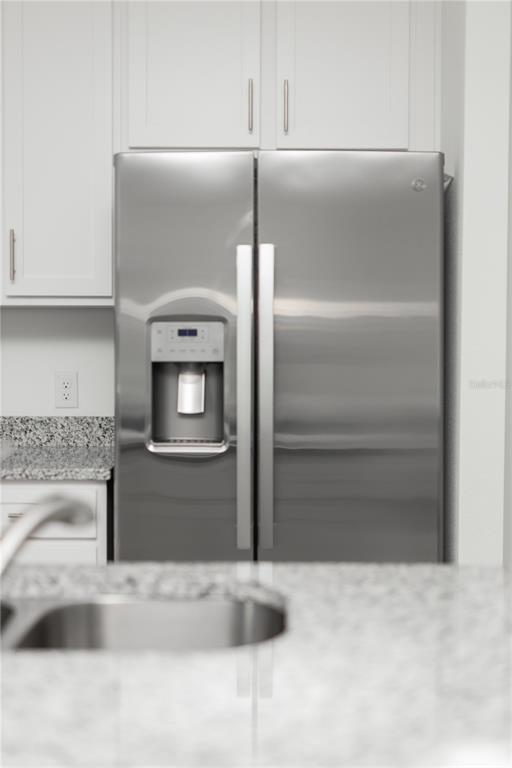 A stainless steel side-by-side refrigerator is positioned next to white cabinets and granite countertops — 661 CROWN ROSE DRIVE, EAGLE LAKE, FL