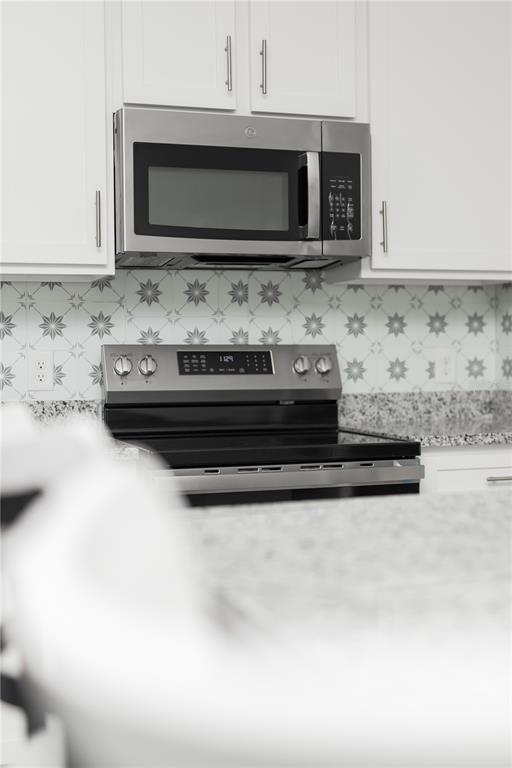 A kitchen features white cabinets, a stainless steel microwave, a black stove, and patterned backsplash — 661 CROWN ROSE DRIVE, EAGLE LAKE, FL