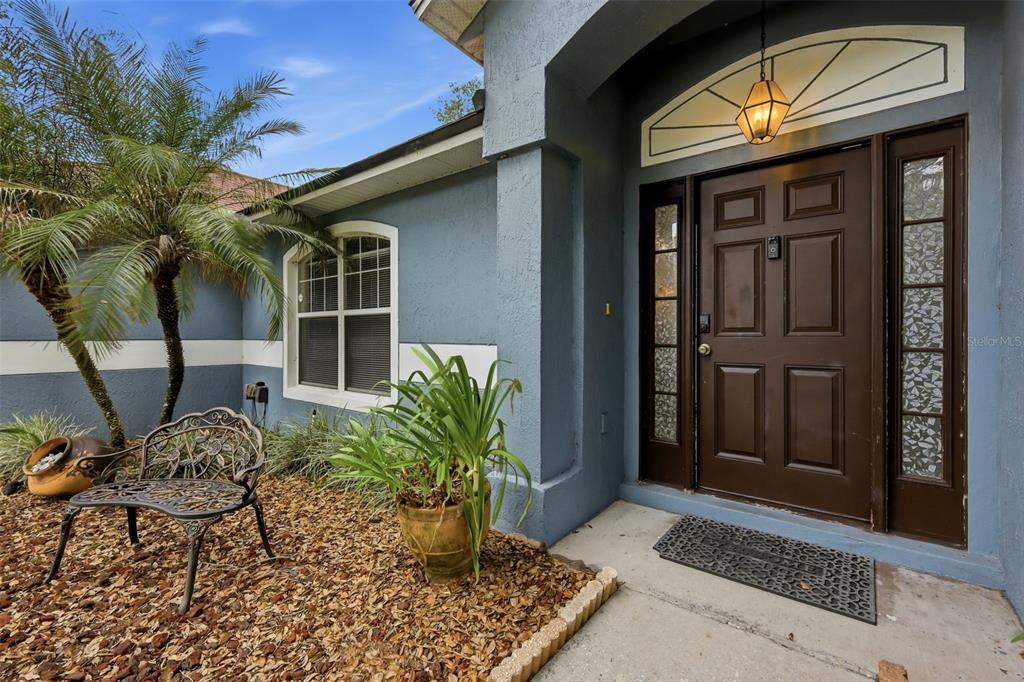 A blue house exterior features a brown front door, a metal bench, and a palm tree — 1313 OAK VALLEY BOULEVARD, MINNEOLA, FL