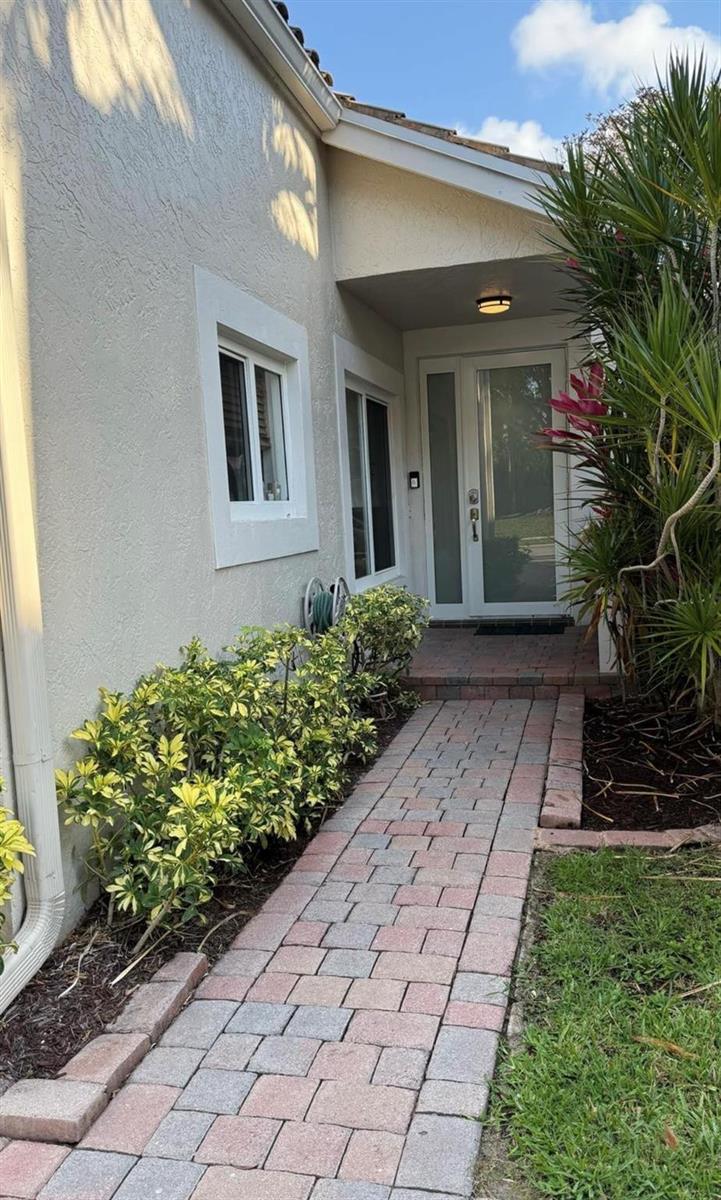 A paved walkway leads to the front entrance of a house with light-colored stucco walls — 6165 NW 77th Place, Parkland FL 33067, PARKLAND, FL