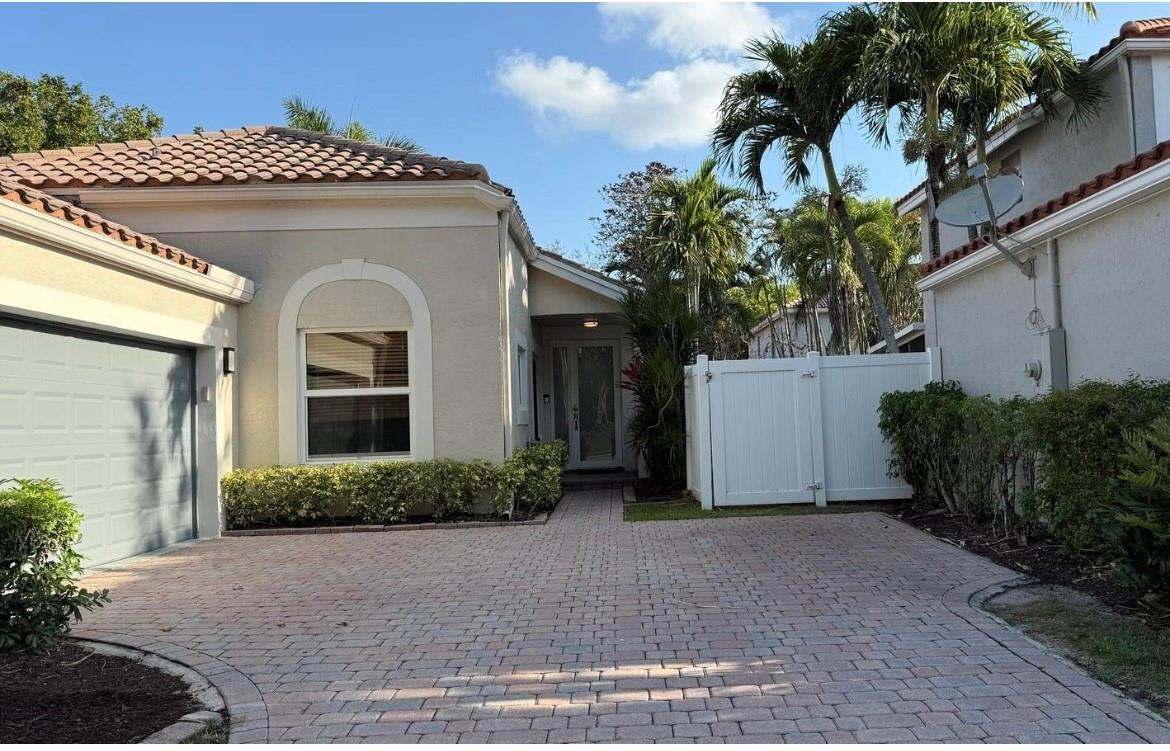 A beige house exterior with a paver driveway, a garage, and a white privacy fence — 6165 NW 77th Place, Parkland FL 33067, PARKLAND, FL