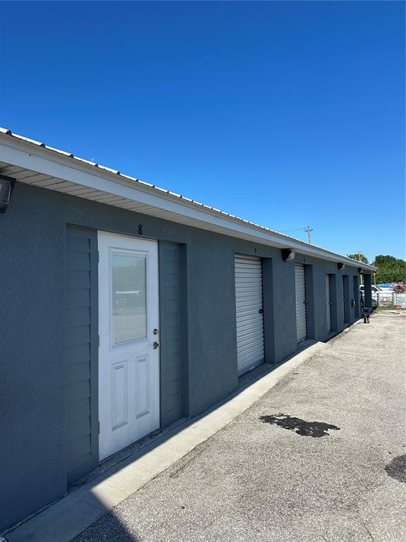 An exterior view of a gray storage building with a white door and roll-up doors — 110 SPIRIT LAKE ROAD UNIT 8, WINTER HAVEN, FL