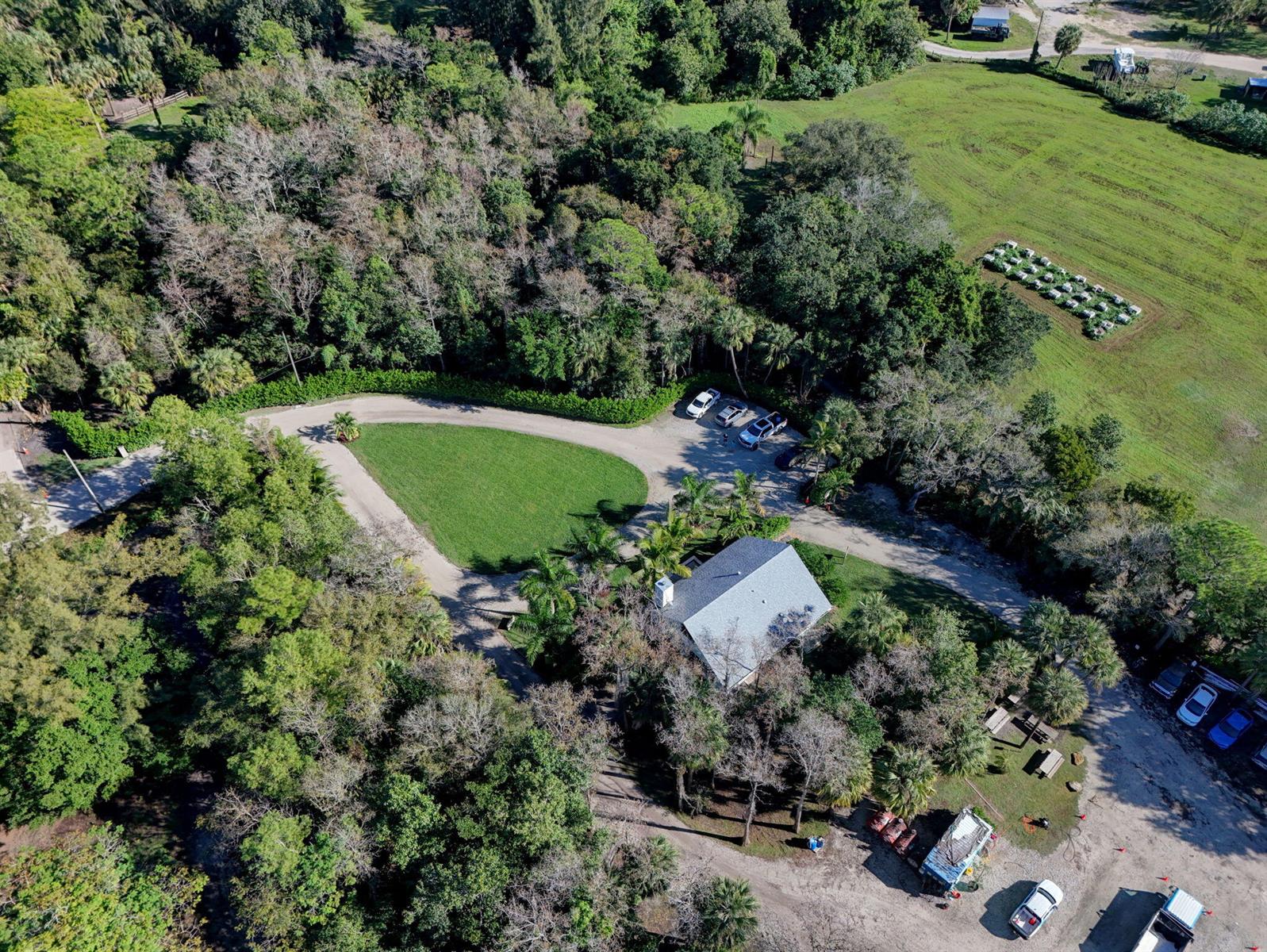 An aerial view shows a house surrounded by trees, a driveway, and a grassy field — 9576 171st Street N, Jupiter FL 33478, JUPITER, FL