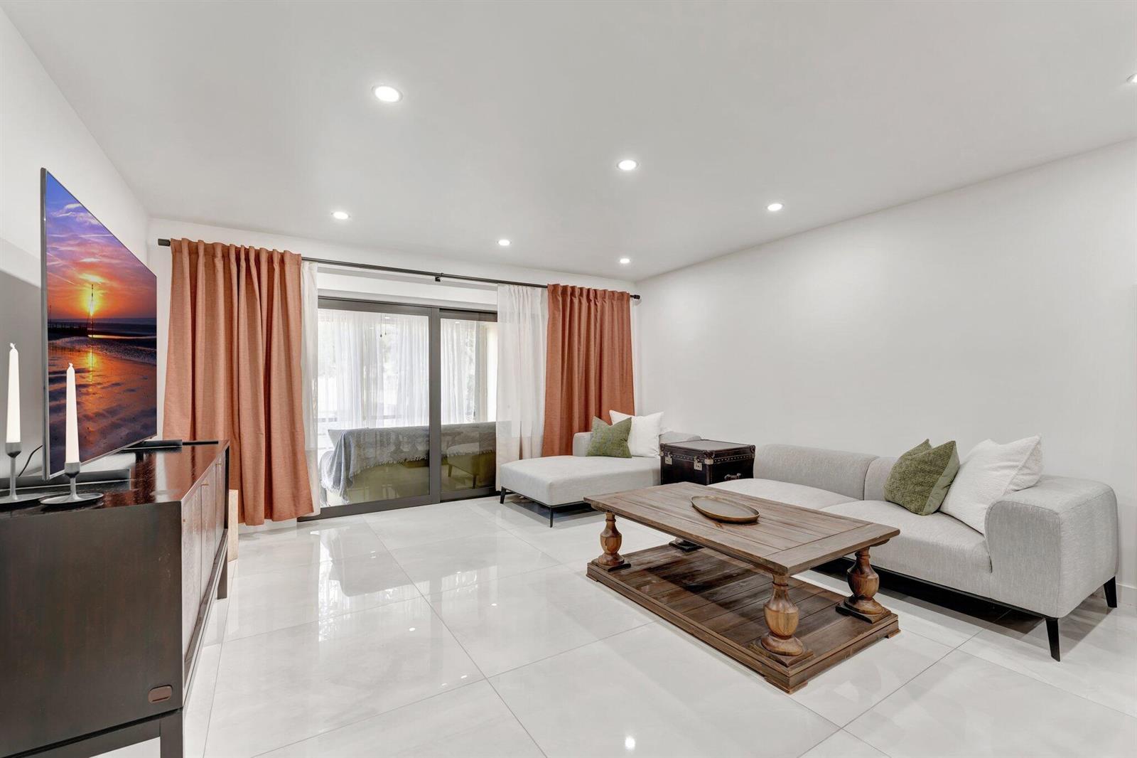 A modern living room features white tile floors, a grey sectional sofa, and sliding glass doors — 138 S Cypress Road # 224, Pompano Beach FL 33060, POMPANO BEACH, FL