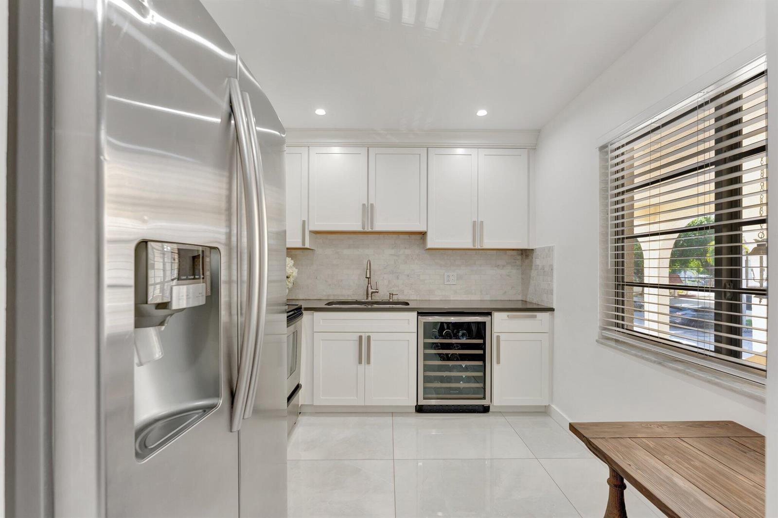 A kitchen with white cabinets, stainless steel appliances, a wine cooler, and light tile flooring — 138 S Cypress Road # 224, Pompano Beach FL 33060, POMPANO BEACH, FL