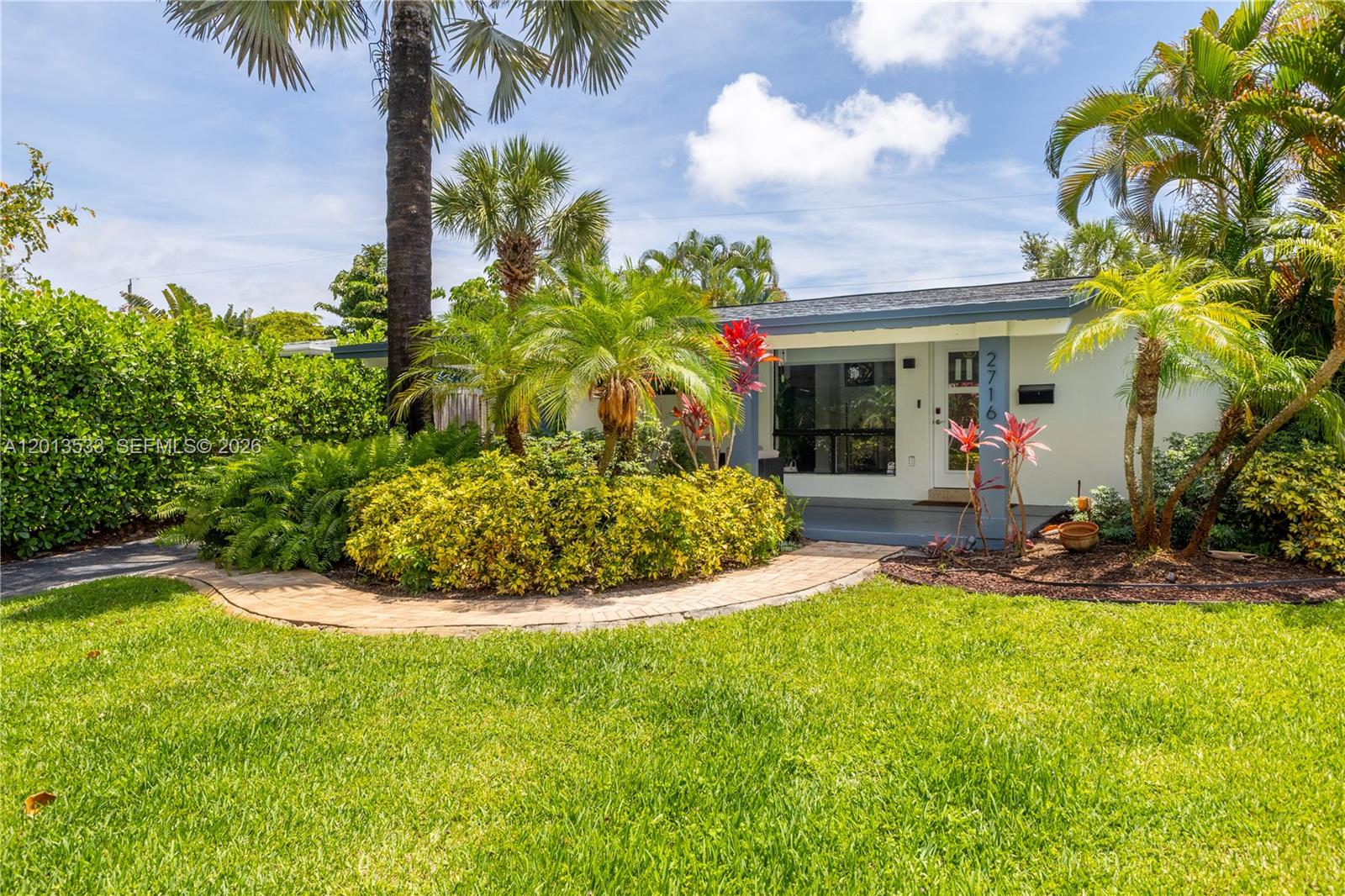 A single-story house with a white exterior, a paved walkway, and lush tropical landscaping — 2716 NW 3rd Ave, Wilton Manors FL 33311, WILTON MANORS, FL