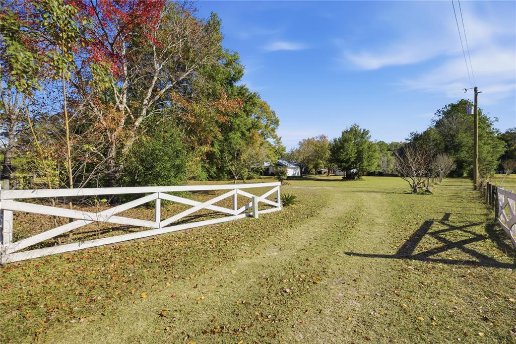 A white wooden fence borders a grassy field leading toward a house in the distance — 18004 NW 55TH PLACE, ALACHUA, FL