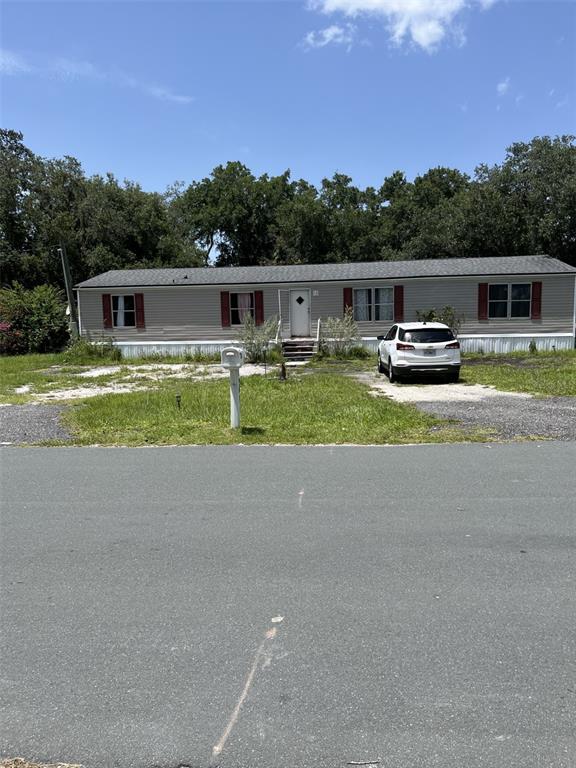 A single-story manufactured home with light siding and red shutters sits behind a gravel driveway — 4901 LILLIAN BLACK ROAD, ST CLOUD, FL