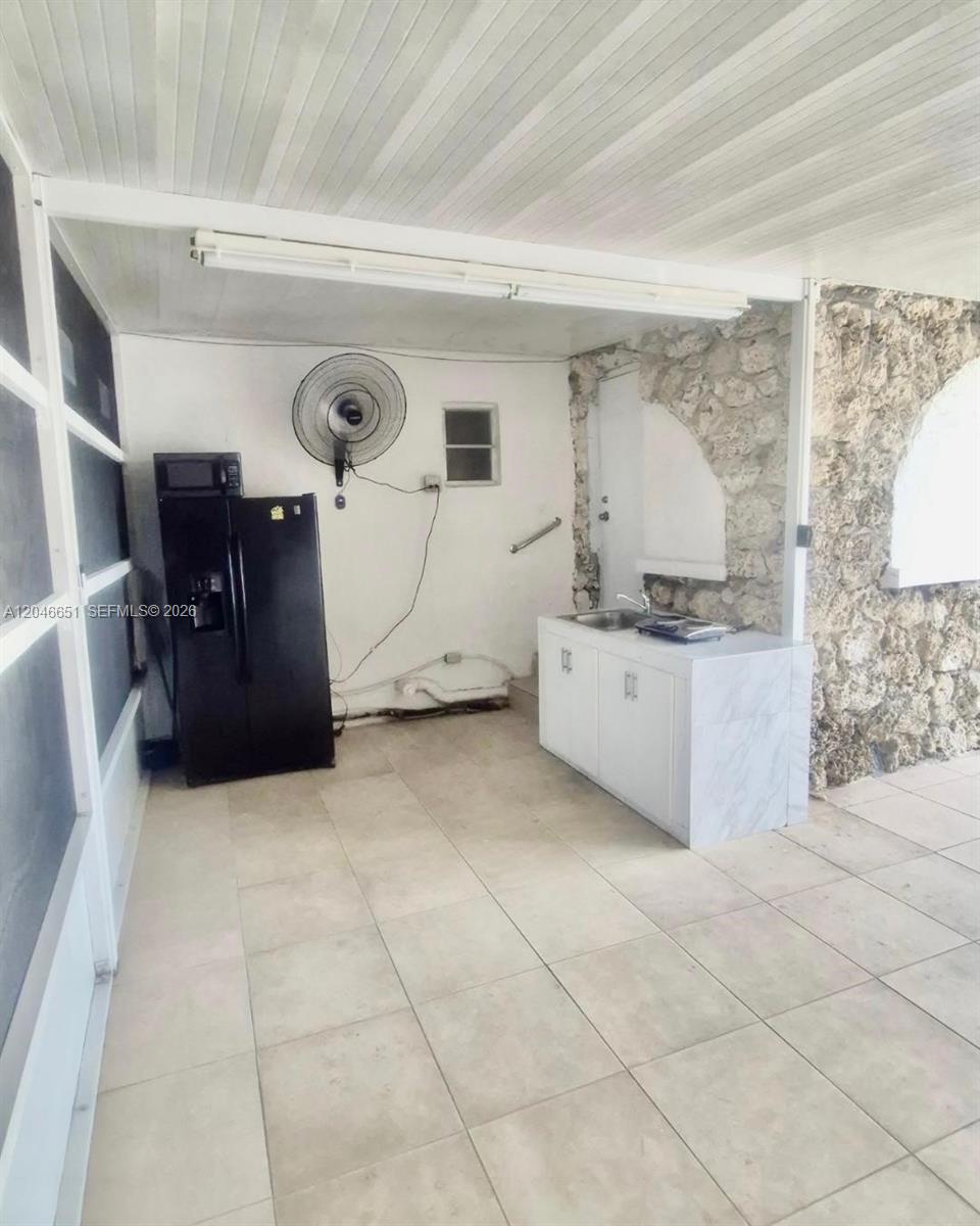 This outdoor kitchen area features a black refrigerator, a small sink cabinet, and stone walls — 1922 NW 4th St # B, Miami FL 33125, MIAMI, FL