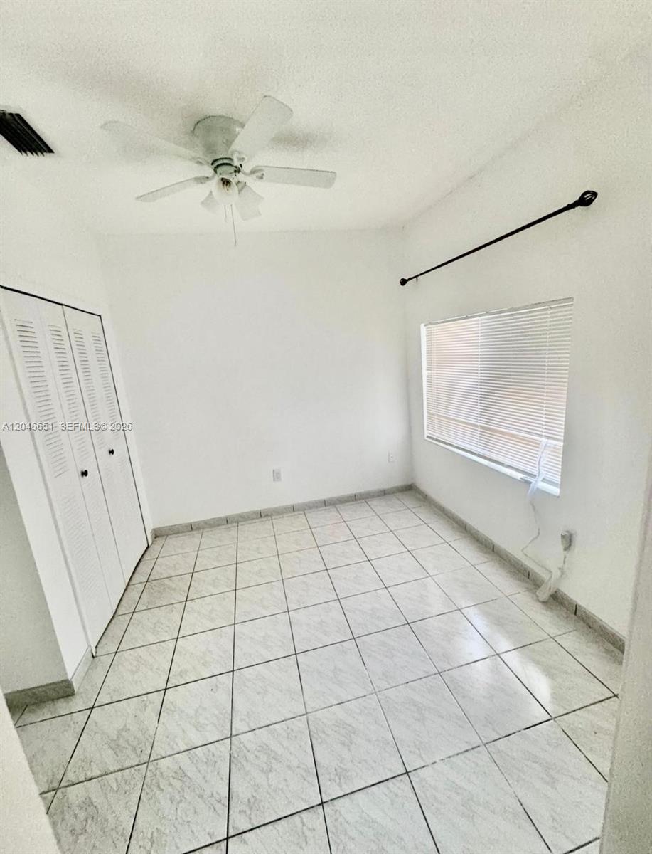 A small, empty bedroom features white walls, tiled floors, a ceiling fan, and a closet — 1922 NW 4th St # B, Miami FL 33125, MIAMI, FL