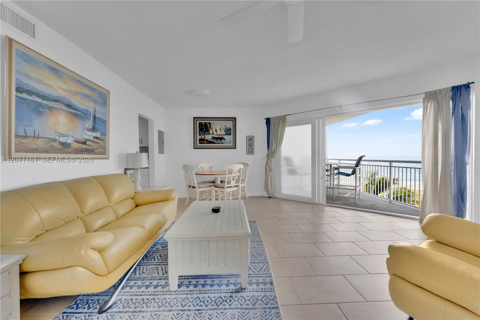 A living room with a yellow sofa, tile floors, and a balcony overlooking the ocean — 710 N Ocean Blvd # 511, Pompano Beach FL 33062, POMPANO BEACH, FL