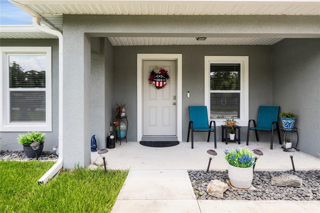 A covered front porch features a light gray door, two blue chairs, and landscaping — 351 W ELM DRIVE, ORANGE CITY, FL