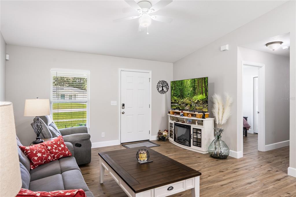 A living room features gray walls, wood-look flooring, a ceiling fan, and a fireplace console — 351 W ELM DRIVE, ORANGE CITY, FL