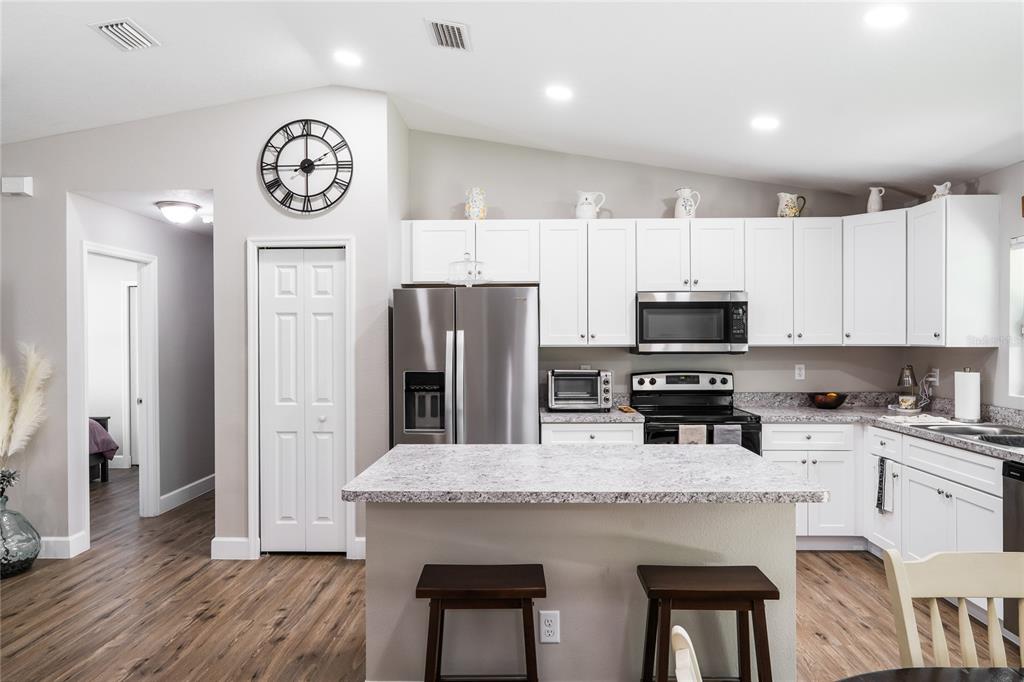 A kitchen features white cabinets, stainless steel appliances, a granite-topped island, and wood-look flooring — 351 W ELM DRIVE, ORANGE CITY, FL