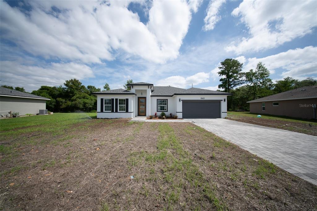 A single-story white house with a dark garage door and a paved driveway — 13621 SW 40TH CIRCLE, OCALA, FL