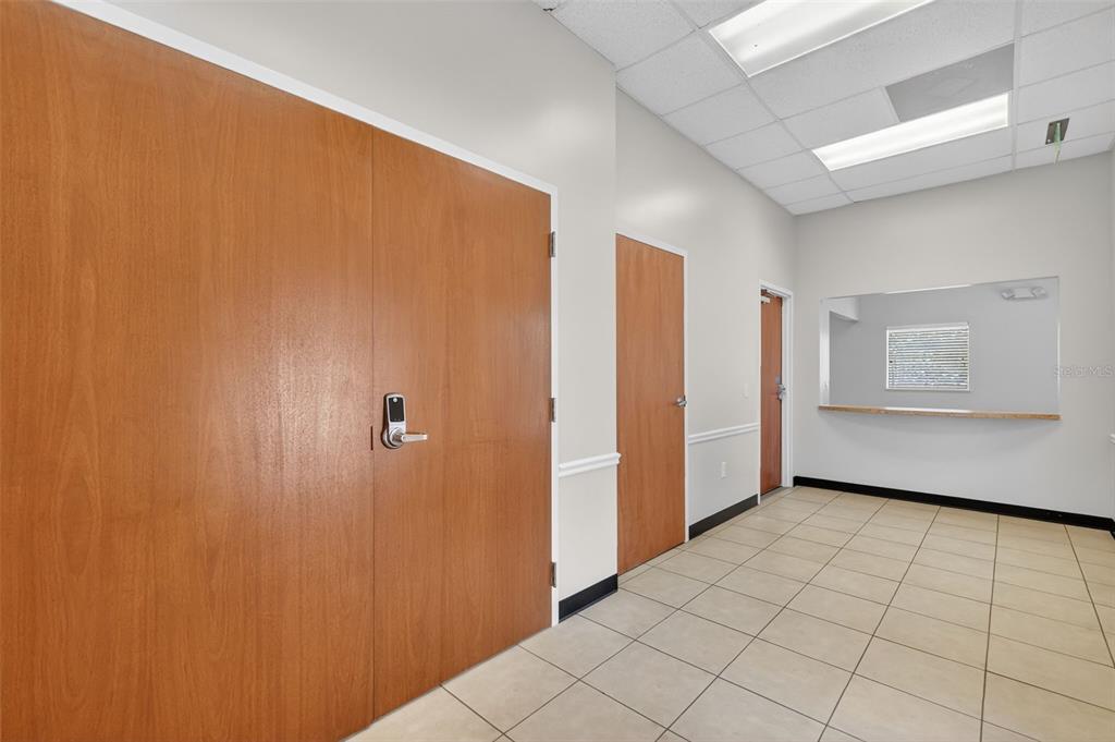 A commercial hallway features light-colored tile flooring, wood-paneled doors, and a service window — 841 OAKLEY SEAVER DRIVE UNIT A, CLERMONT, FL