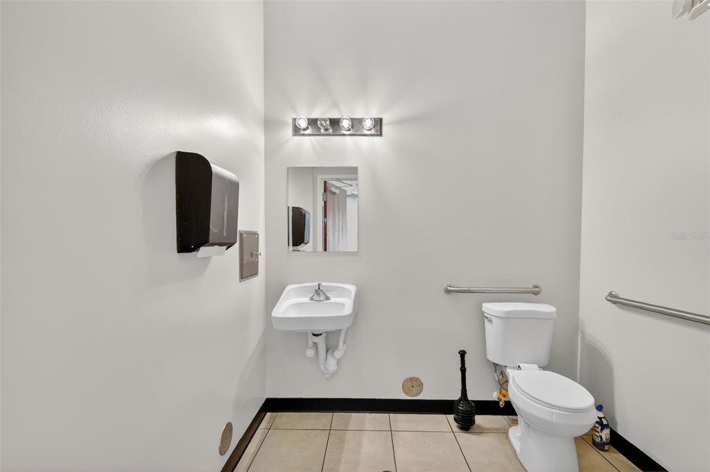A small, white-walled commercial restroom features a wall-mounted sink, toilet, and grab bars — 841 OAKLEY SEAVER DRIVE UNIT A, CLERMONT, FL