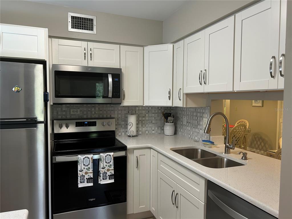 A kitchen features white cabinets, stainless steel appliances, a tiled backsplash, and light-colored countertops — 5662 GARDENS DRIVE UNIT 104, SARASOTA, FL
