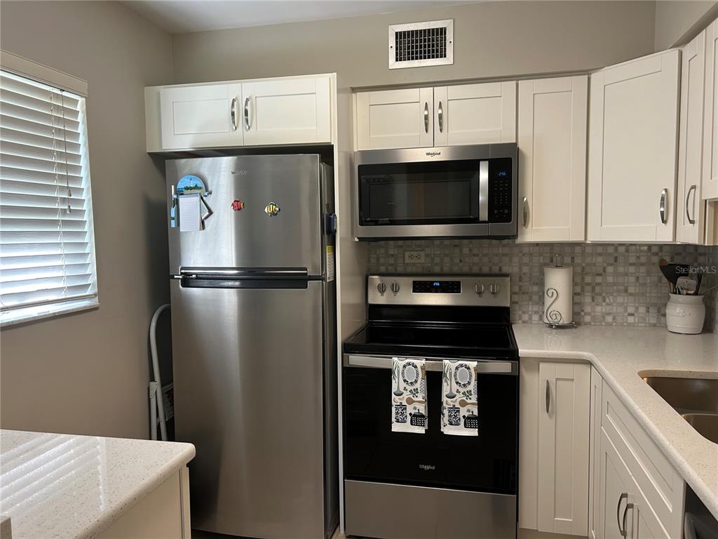 A kitchen features white cabinets, stainless steel appliances, and a tiled backsplash — 5662 GARDENS DRIVE UNIT 104, SARASOTA, FL